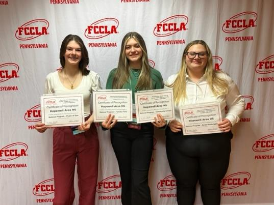 Three students sitting holding certificates